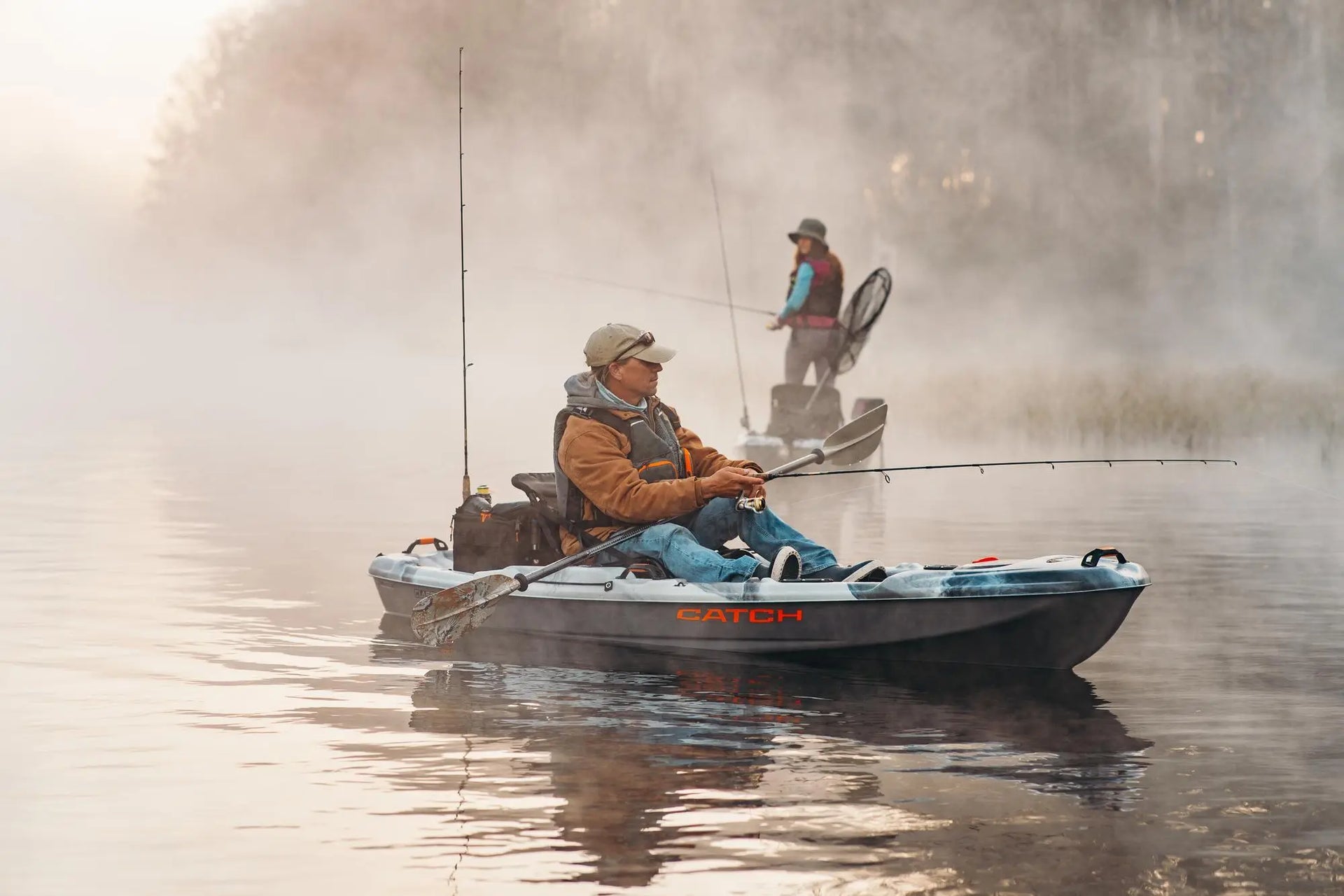 Two anglers fishing from Pelican Catch kayaks on a foggy lake at sunrise.
