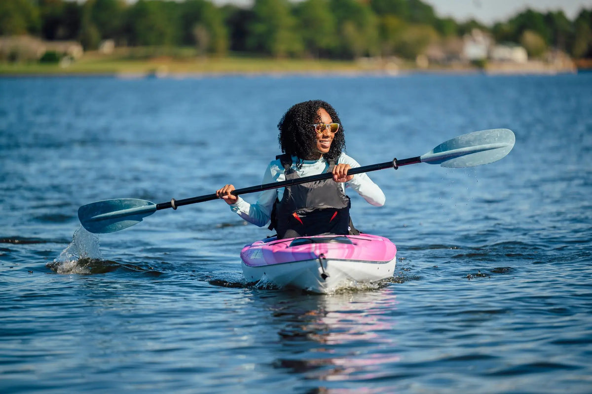 A woman paddling a pink and white Pelican Argo 100X kayak on open water.